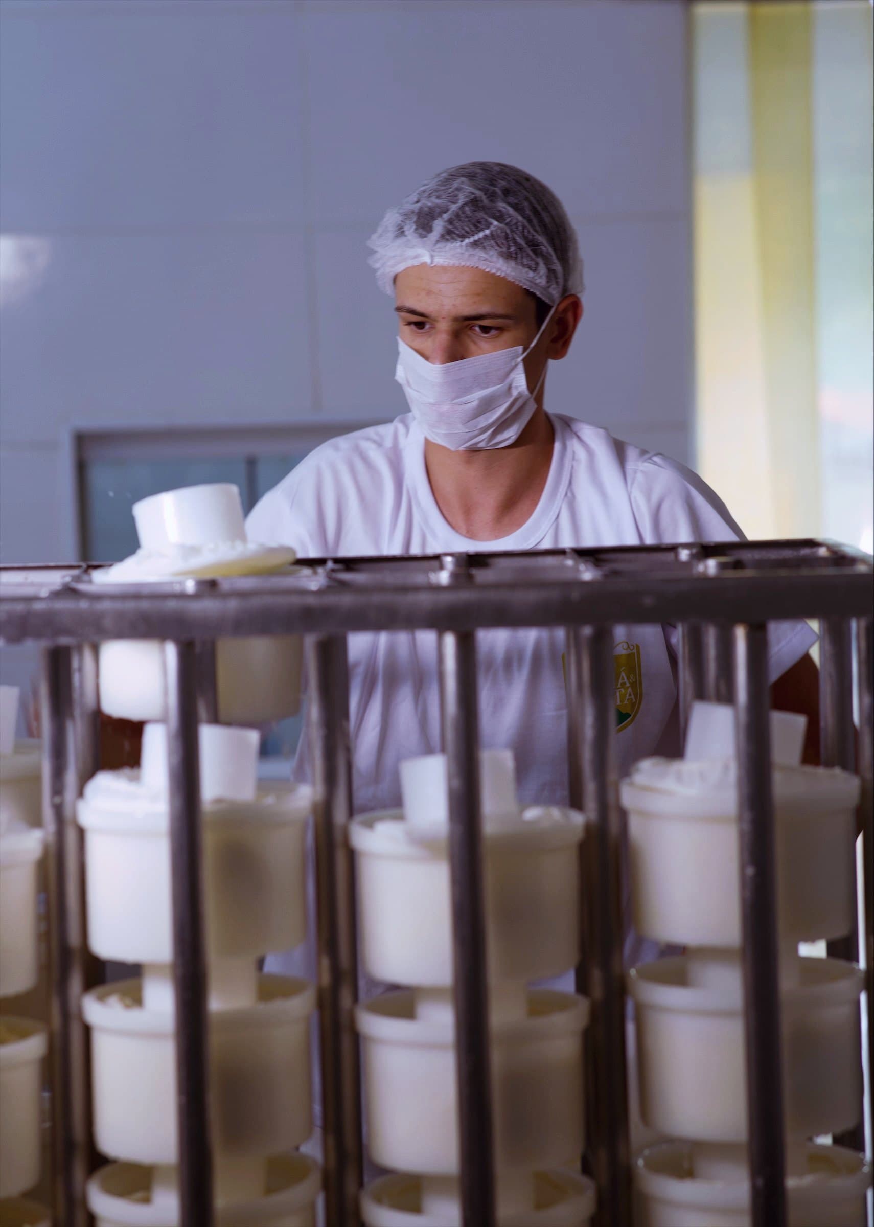 Funcionário de touca e máscara organizando as formas de queijo